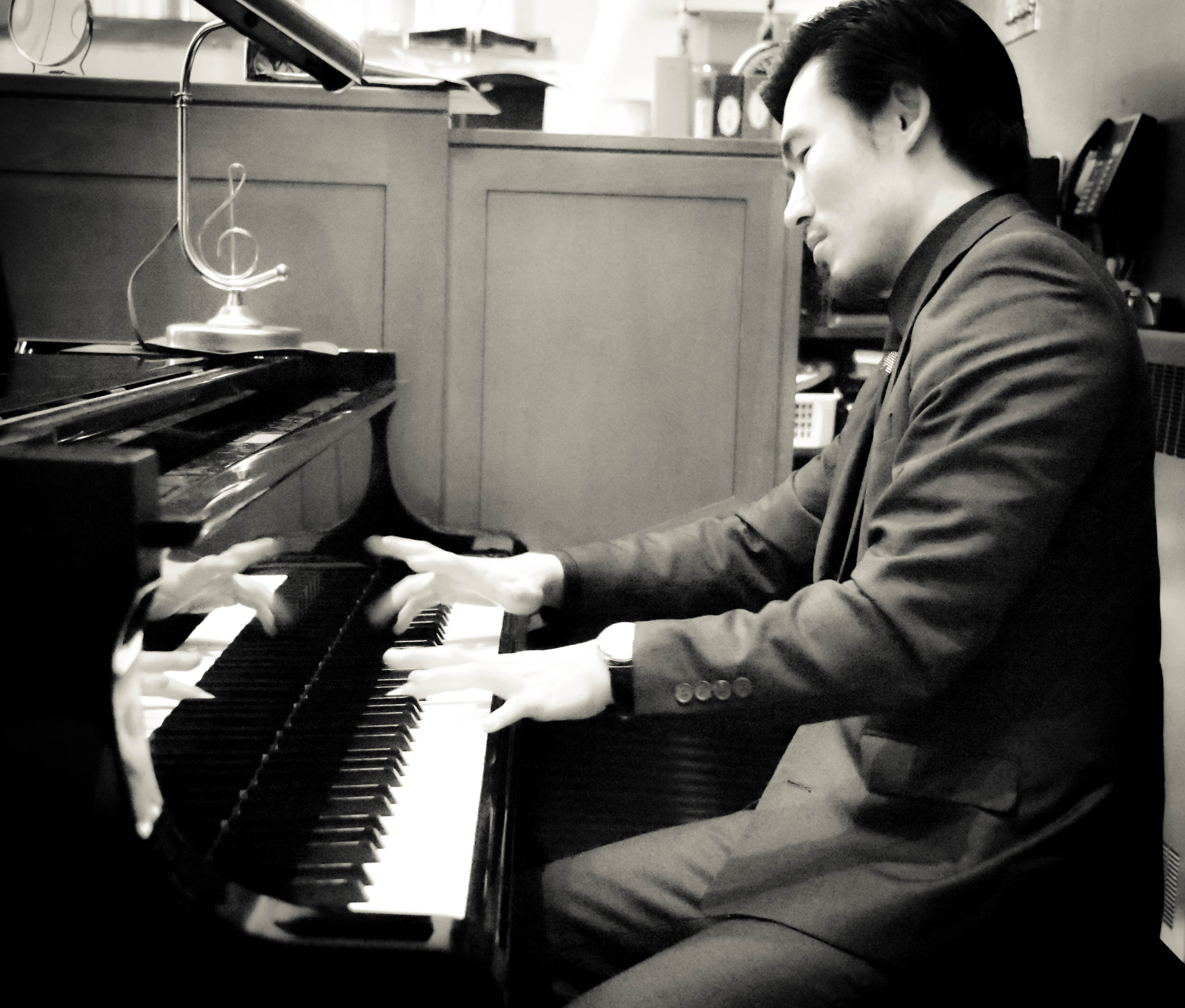 A profile shot of Sebastian playing the piano in black and white